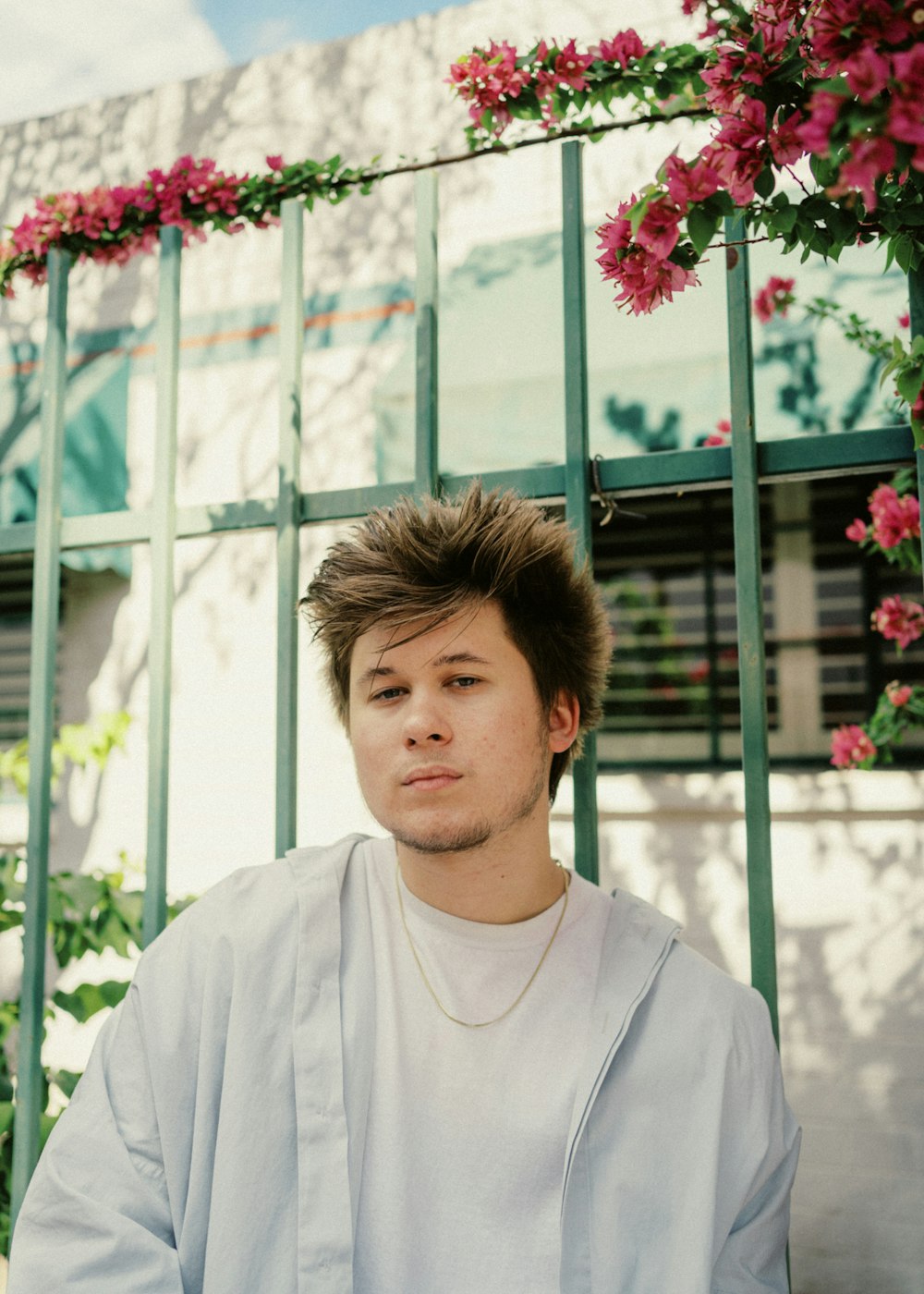 man in white crew neck shirt standing near red flowers