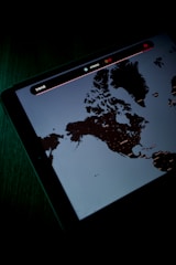 A digital screen displaying a map, possibly of Northern regions, with text and icons above the map. The screen is emitting a dim light, creating a contrast against the dark surroundings.