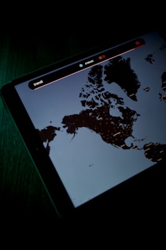 A digital screen displaying a map, possibly of Northern regions, with text and icons above the map. The screen is emitting a dim light, creating a contrast against the dark surroundings.