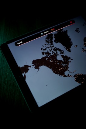A digital screen displaying a map, possibly of Northern regions, with text and icons above the map. The screen is emitting a dim light, creating a contrast against the dark surroundings.