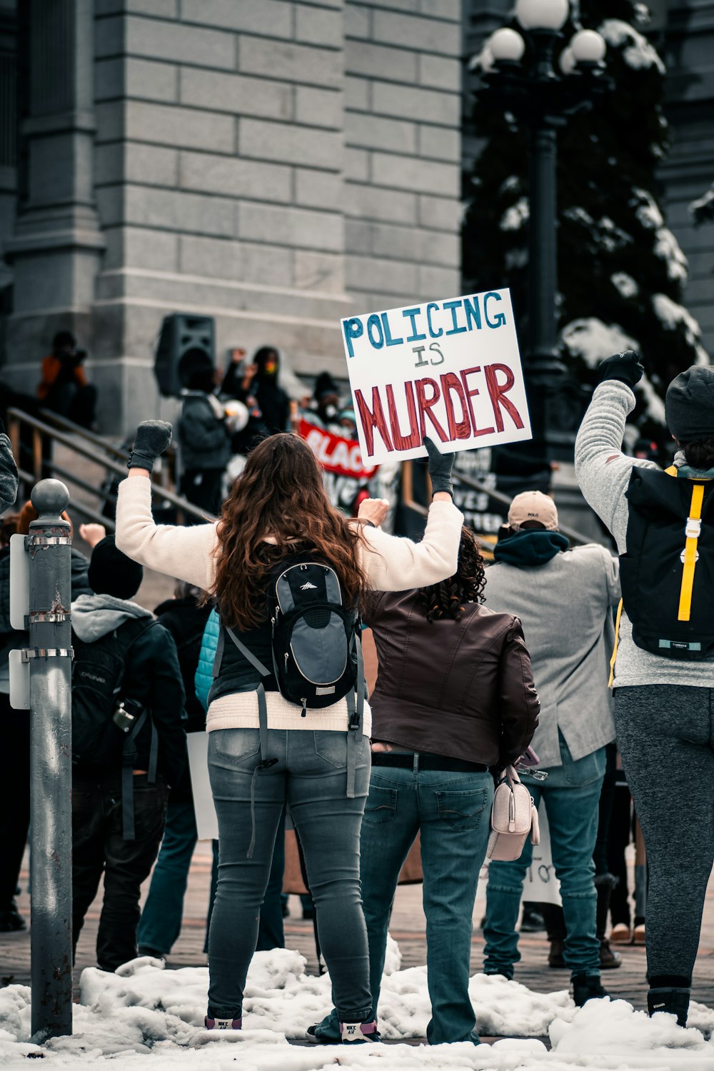 woman in black jacket and blue denim jeans standing near people walking on street during daytime