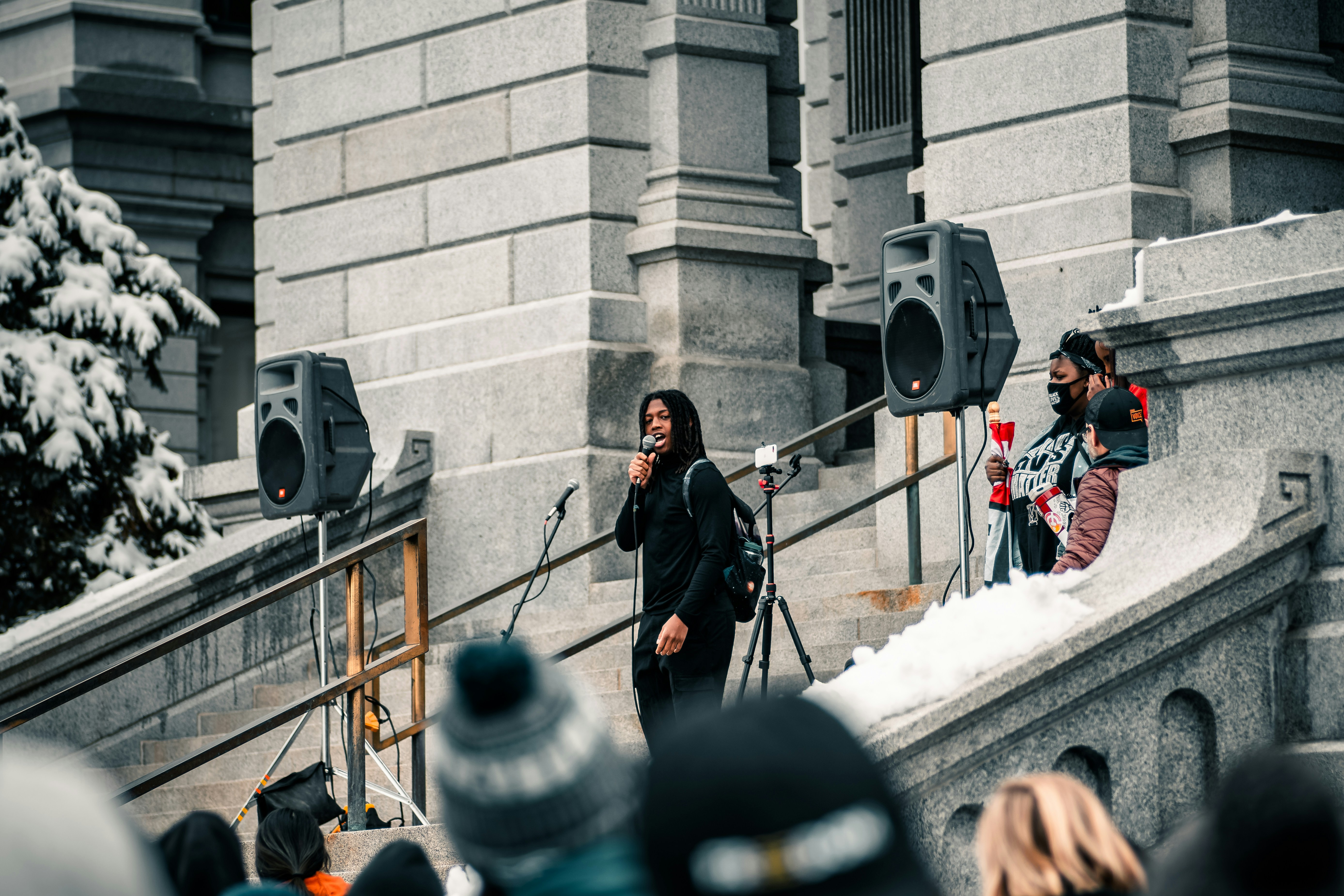 man in black coat standing beside black and gray speaker, 