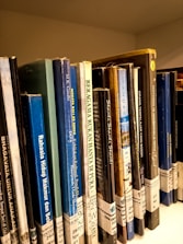 A collection of colorful Wolof language books displayed on a wooden shelf.