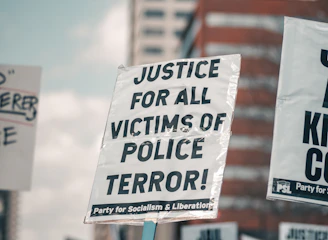 A close-up of a protest sign highlighting police misconduct in a crowded city street.