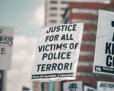 A close-up of a protest sign highlighting police misconduct in a crowded city street.