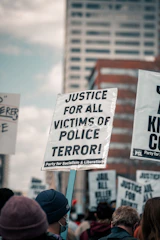 A close-up of a protest sign highlighting police misconduct in a crowded city street.