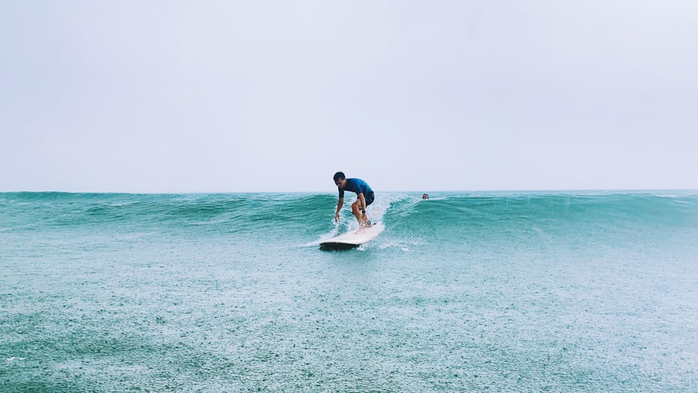 昼間、海で白いサーフボードに乗る青いシャツと黒いショートパンツの男