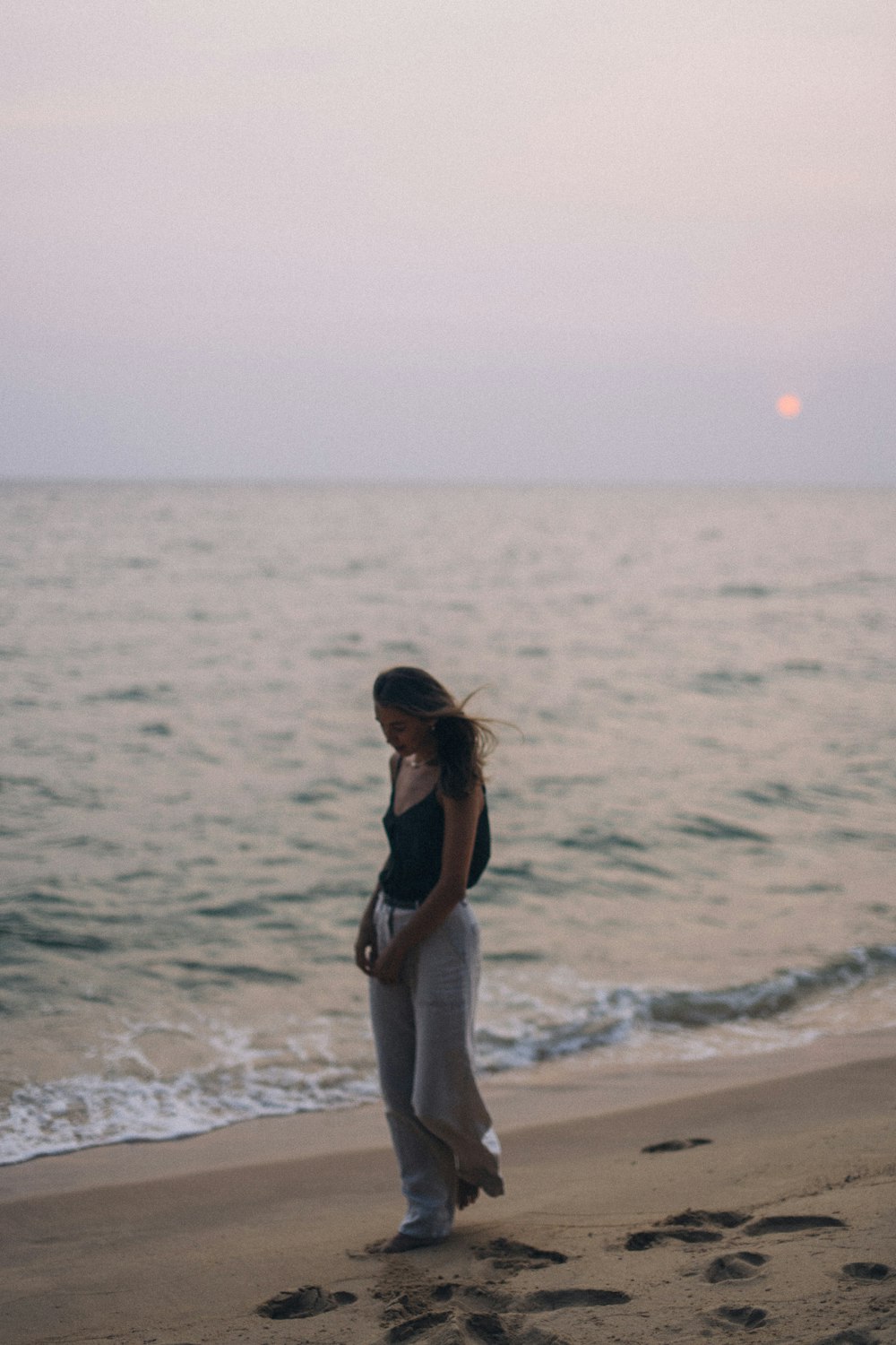 donna in canotta bianca e nera e pantaloni bianchi in piedi sulla spiaggia durante il giorno
