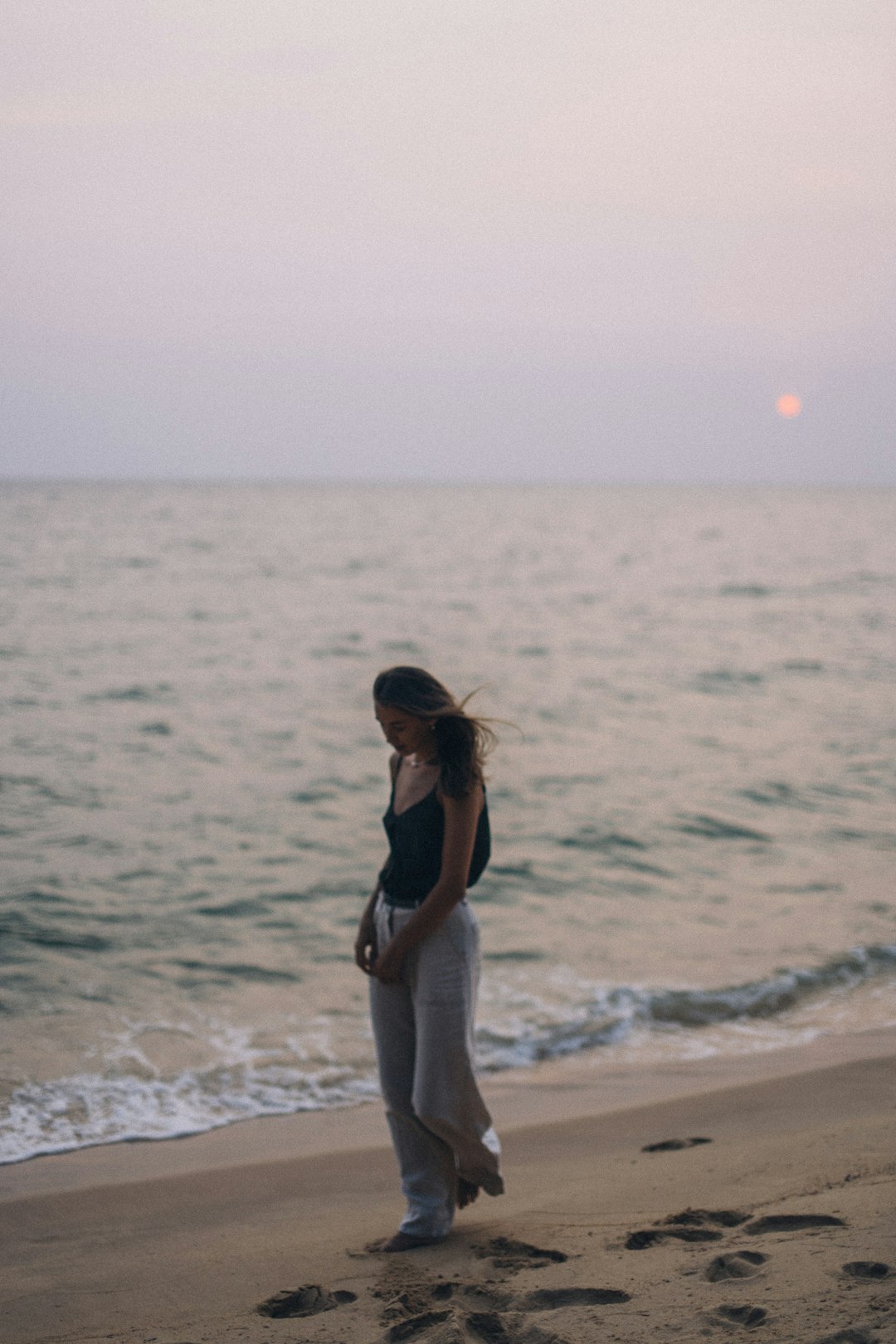 woman in black and white tank top and white pants standing on beach during daytime