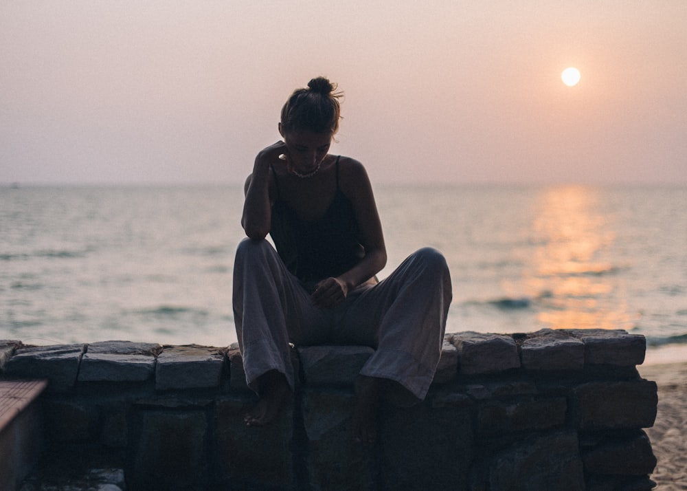 woman in black shirt sitting on concrete bench near sea during daytime