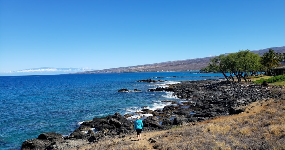 person in blue jacket standing on rock formation near body of water during daytime