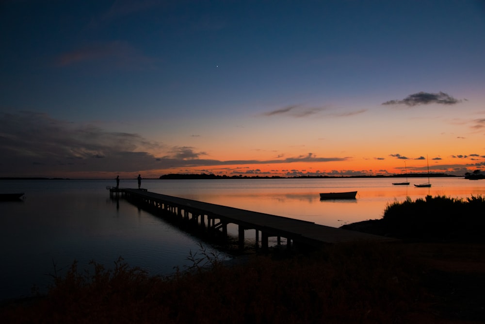 brown wooden dock on body of water during sunset