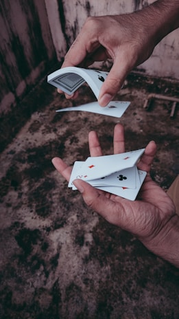 A person skillfully performs a card trick, showing playing cards spread between their hands. The background is a textured, weathered surface, adding a rustic feel.