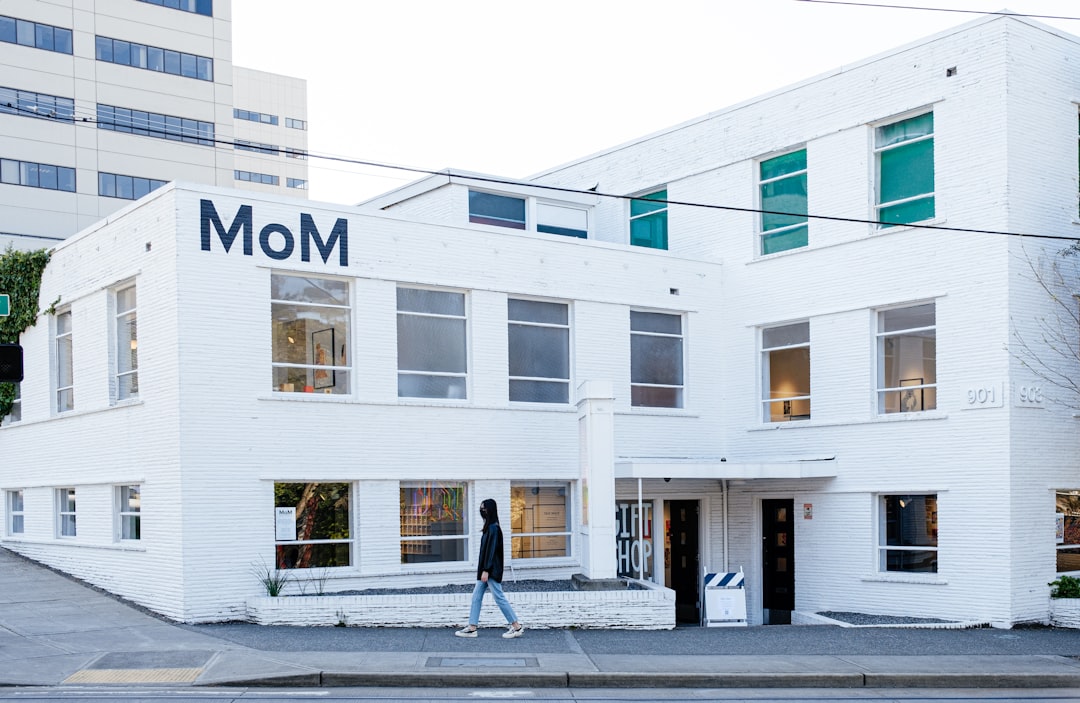 woman in black jacket walking on sidewalk near white concrete building during daytime