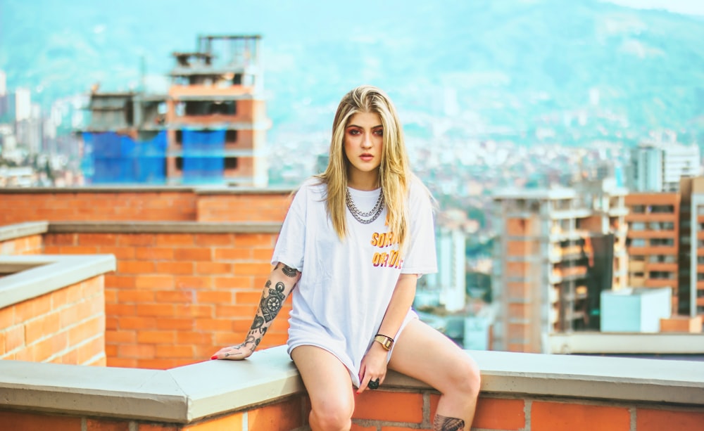 woman in white crew neck t-shirt sitting on brown wooden bench during daytime