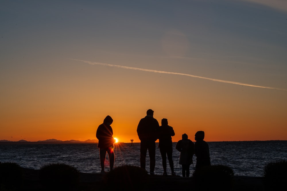 silhouette of people standing on seashore during sunset