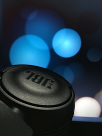 A close-up view of a black JBL headphone with a blurred background featuring large blue bokeh circles.