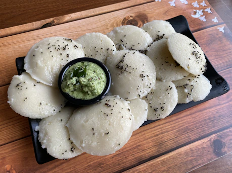 A vibrant plate of traditional Bengali panta bhat with fresh green chilies and onions on a rustic wooden table.