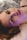 A person is lying down with a serene expression, illuminated by a soft, colorful light that casts purple and pink hues on their face. The background is blurred, creating a gentle atmosphere.