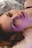 A person is lying down with a serene expression, illuminated by a soft, colorful light that casts purple and pink hues on their face. The background is blurred, creating a gentle atmosphere.