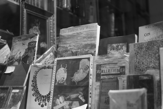 A collection of books and magazines is displayed, each with unique cover art and typography. Some covers feature historical illustrations, while others show text in various languages. The image is in black and white, enhancing the vintage and classic appearance of the publications.
