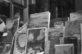 A collection of books and magazines is displayed, each with unique cover art and typography. Some covers feature historical illustrations, while others show text in various languages. The image is in black and white, enhancing the vintage and classic appearance of the publications.