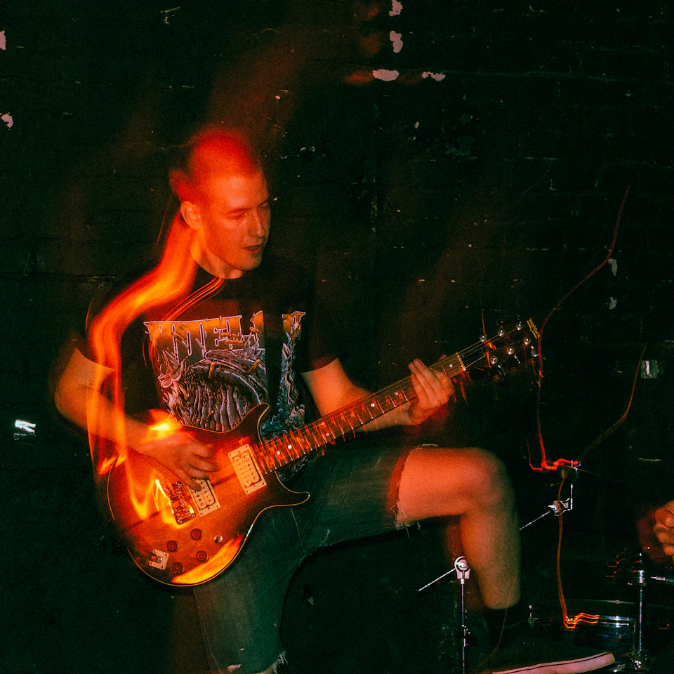 Man plays electric guitar with glowing flame design in dimly lit room setting