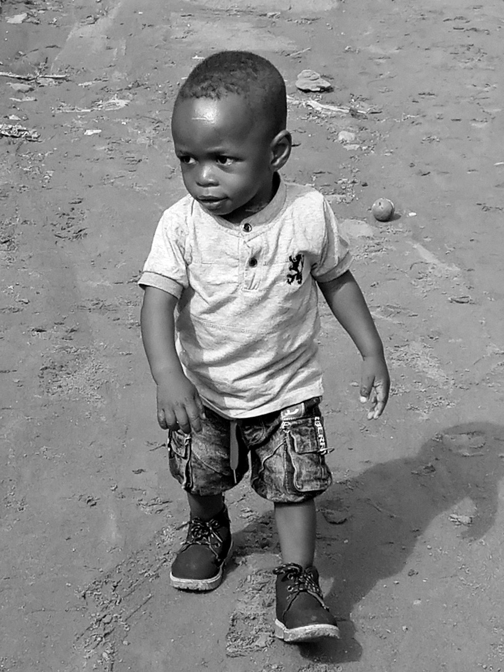 grayscale photo of child in white t-shirt and blue denim shorts standing on sand