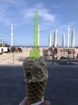A colorful scoop of creamy gelato in a waffle cone with a sunny coastal backdrop.