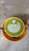 Close-up of a delicate matcha latte in a pastel yellow cup with a swirl of cream.