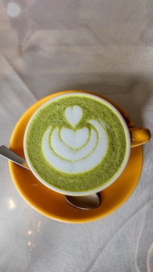 Close-up of a delicate matcha latte in a pastel yellow cup with a swirl of cream.