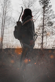 Close-up of weathered hands holding a bow with a forest backdrop.