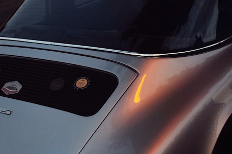 Close-up of a vintage luxury car's polished chrome grille and emblem, reflecting a sunset.