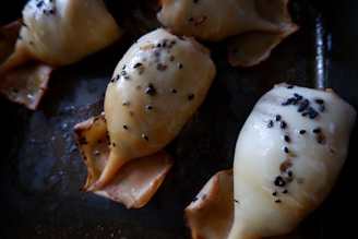 A close-up view of baked dumpling-like pastries with a golden-brown top. They are sprinkled with black sesame seeds and arranged on a dark baking sheet.