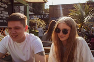 Couple enjoying a sunny outdoor café with yellow accents in the background.