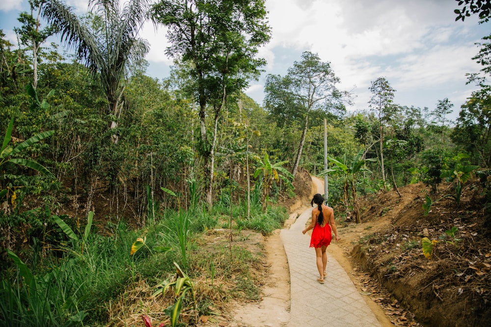 빨간 드레스를 입은 여자가 낮에 푸른 풀과 나무 사이의 오솔길을 걷고 있습니다.