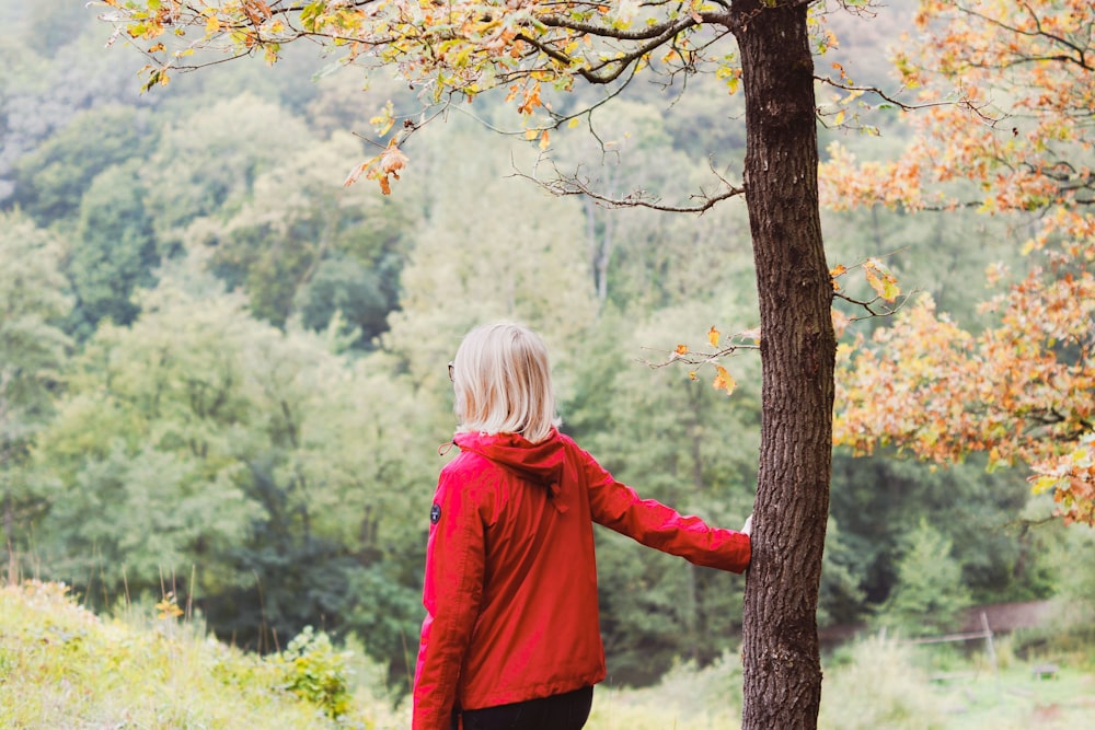 girl in red jacket standing beside brown tree during daytime