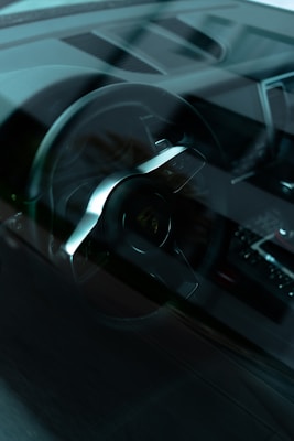 A close-up interior view of a car showcasing the steering wheel and part of the dashboard. The image has a reflective surface, indicating it was taken through a car window. The design elements suggest a modern and sophisticated vehicle.