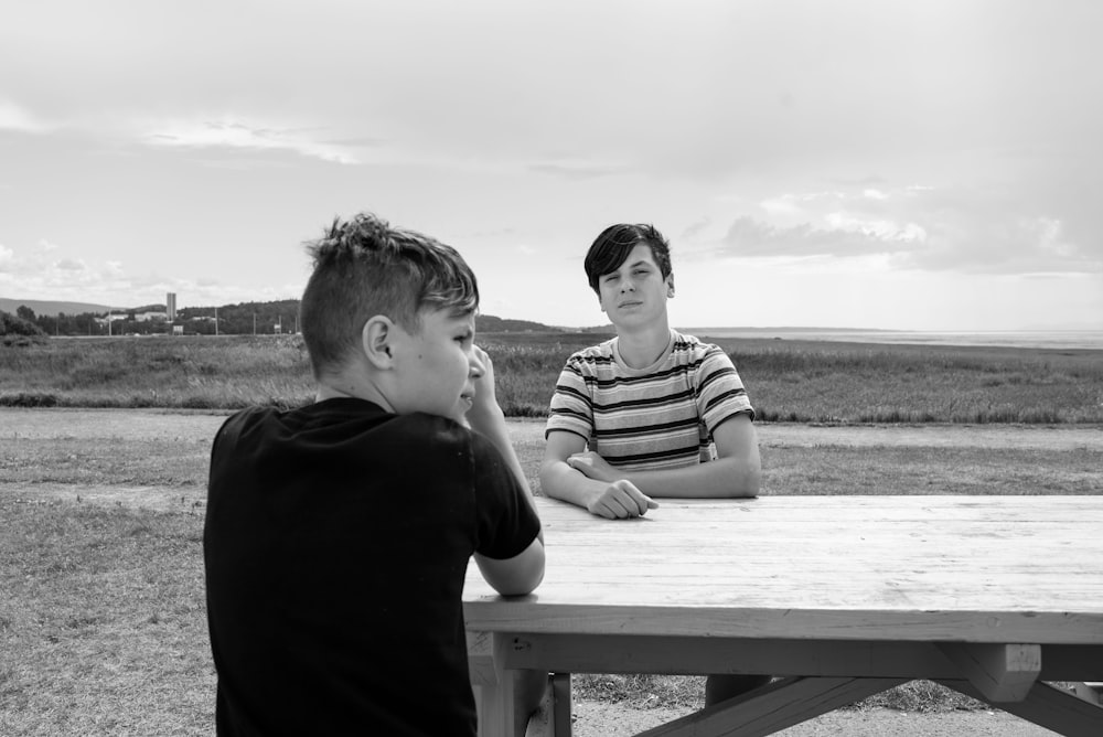 grayscale photo of boy and girl sitting on wooden bench