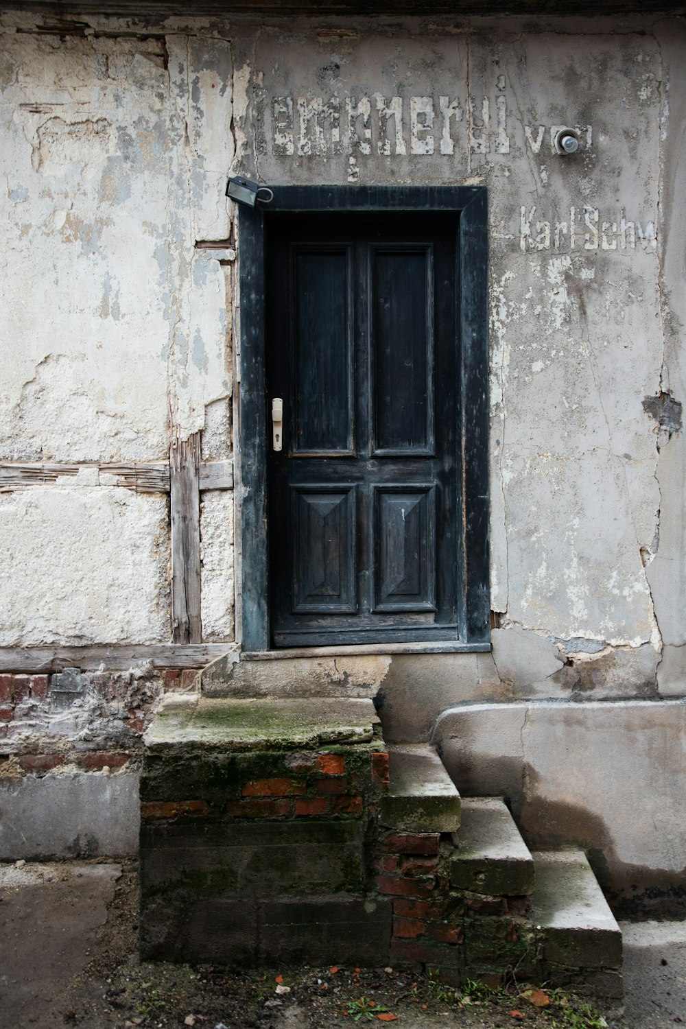 白いコンクリートの壁に黒い木製のドア