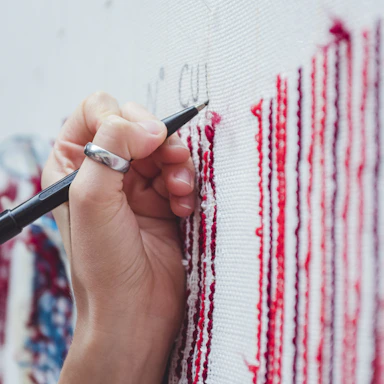 A close-up photo of a hand sketching a rebellious figurative artwork with red and black ink.