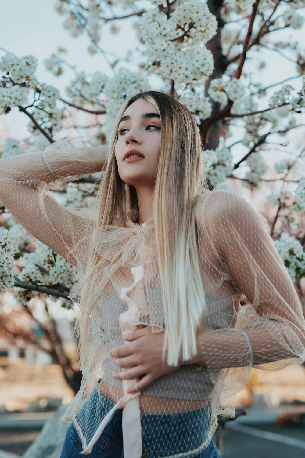 woman in white lace long sleeve shirt standing under white cherry blossom tree during daytime