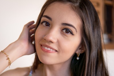 Elegant woman wearing subtle gold earrings and a bracelet, smiling softly in natural light.