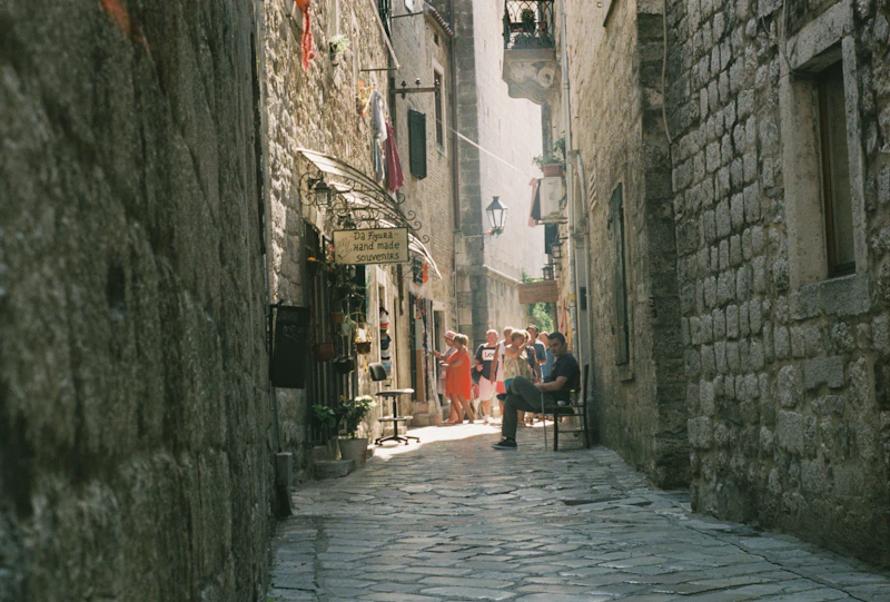 A narrow stone lane in Kotor's Old Town with people and a belltower in the distance