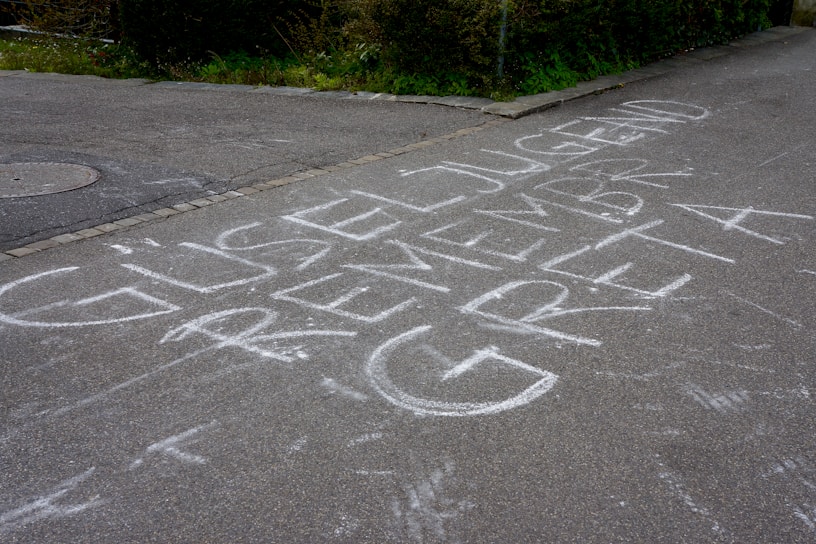 Chalk writing on a pavement spells out a message that includes the words 'GÜSELJUGEND' and 'REMEMBER GRETA'. The letters are large and white, covering a significant portion of the ground.