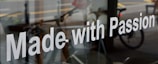The image features a glass window with the phrase 'Made with Passion' prominently displayed in white text. Behind the glass, there is a blurred view of a street scene, including a bicycle and some indistinct urban elements.