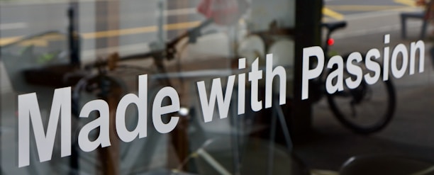 The image features a glass window with the phrase 'Made with Passion' prominently displayed in white text. Behind the glass, there is a blurred view of a street scene, including a bicycle and some indistinct urban elements.