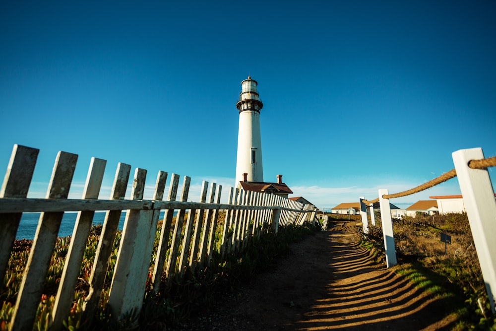 Weißer und schwarzer Leuchtturm in der Nähe von Meer unter blauem Himmel tagsüber