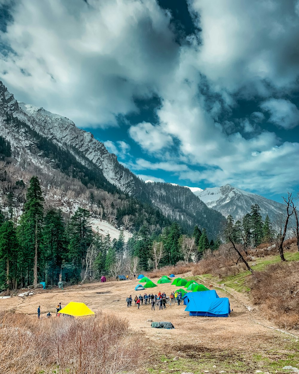 tenda verde e gialla vicino agli alberi verdi e alla montagna sotto le nuvole bianche ed il cielo blu durante