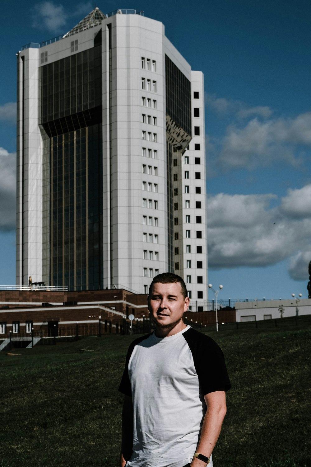 man in black jacket standing on green grass field near high rise building during daytime